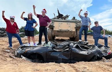 John Nesbit and his family standing on a crushed car in front of an armored vehicle at Tank Town in North Georgia